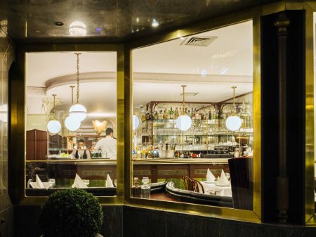 Foto de París, Francia - Nov 2022: camarero camarero organizando las botellas vasos en un restaurante de lujo - vista desde la calle del bar - Imagen libre de derechos