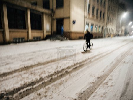 Photo for Defocused silhouette view of a lonely man cycling on a snowy road in city - snow storm with powerful winds - Royalty Free Image