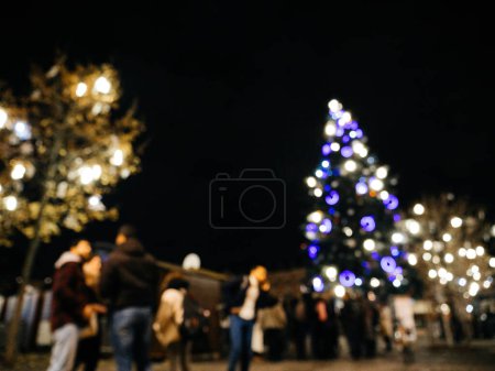 Foto de Vista desenfocada de personas peatones admirando el mercado navideño con abeto alto iluminado en la plaza central de la ciudad - Imagen libre de derechos