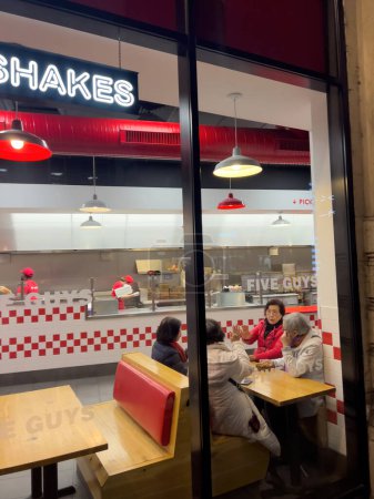 Photo for Strasbourg, France - nov 11, 2022: Friday night - Asian ethnicity friends women talking at the wooden table inside Five Guys fast food restaurant - Royalty Free Image