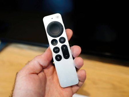Foto de Paris, France - Oct 28, 2022: Male hand close-up of new Apple Computers Siri Remote voice recognition of new Apple TV 4K touch-enabled clickpad in front of tv - defocused background - mute button - Imagen libre de derechos