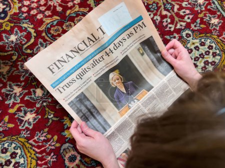 Téléchargez les photos : London, United Kingdom - FEb 2, 2022: Directly above view of woman reading on the living room silk rug floor latest Financial Times with headline Liz Truss quits after 44 days as British Prime - en image libre de droit