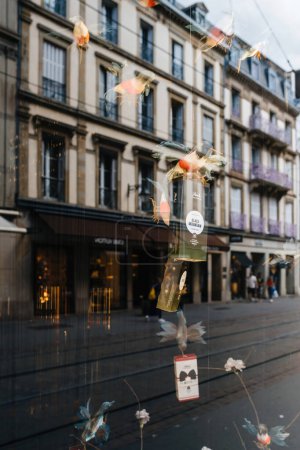 Foto de Strasbourg, France - Sep 9, 2022: colibri birds holding Reck Cafe for nespresso aluminum pods - view inside the showcase of the iconic store with tall building reflect in background - Imagen libre de derechos