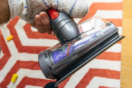 Foto de Paris, France - Jul 4, 2022: POV male hand with bandaged finger holding front view modern new Dyson anti-tangle conical brush bar picks up long hair and pet hair. Fast. Motor-driven cleaning for small - Imagen libre de derechos
