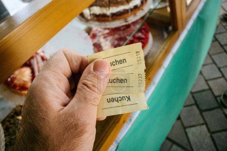 Téléchargez les photos : Male hand holding generic tickets with Kuchen german word printed translated as Cake - delicious pastries background - en image libre de droit
