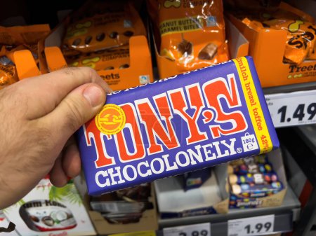 Foto de Dortmund, Germany - Feb 19, 2022: POV male hand holding package pack with Tonys Chocolonely toffee chocolate with shelves in supermarket in background - Imagen libre de derechos