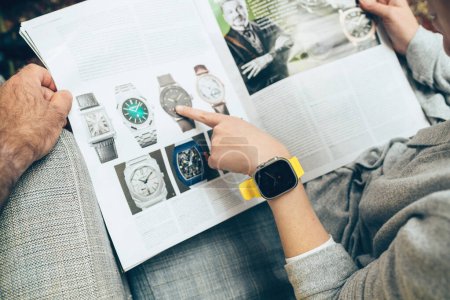 Photo for London, United Kingdom - Sept 28, 2022: Woman and man reading large watch advertising inside How To Spend It HTSI by Financial Times she is wearing new Apple Watch Ultra by Apple Computers on her - Royalty Free Image