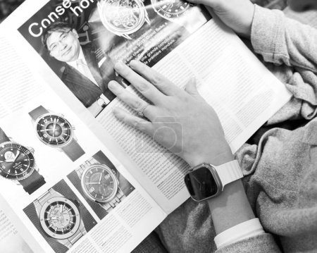 Foto de London, United Kingdom - Sept 28, 2022: Black and white image Fashionable woman looking at large watch advertising inside How To Spend It HTSI by Financial Times wearing new Apple Watch Ultra by Apple - Imagen libre de derechos