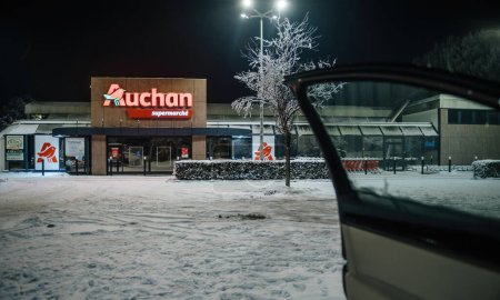 Foto de Strasbourg, France - Dec 19, 2022: Closed Auchan supermarket late at night seen through open door of a car - covered with snow asphalt parking - Imagen libre de derechos