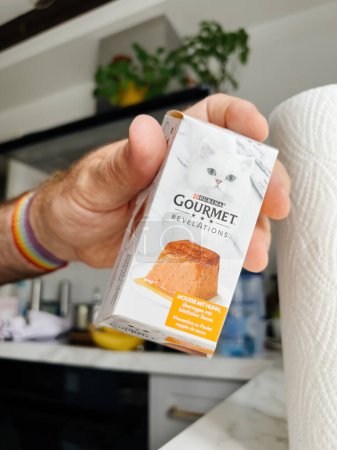 Foto de Paris, France - Sep 13, 2022: POV male hand holding Purina gourmet with wet cat food Jelly with taste - modern kitchen background preparing to feed the pet cat animal - Imagen libre de derechos