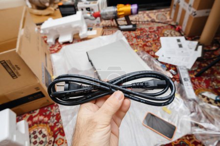 Photo for Paris, France - Dec 13, 2022: POV male hand holding power cable after unboxing new Onkyo NS-6170 network audio player with DSD Hi-Res Audio and DSD DAB WIFI device carpet rug silk background - Royalty Free Image
