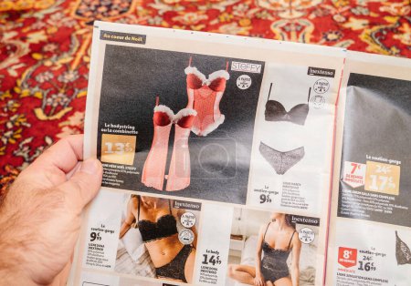 Téléchargez les photos : Paris, France - Dec 2, 2022: Man reading Auchan France leaflets supermarket chain selling underwear for women by Inestenso and Steffy brand - en image libre de droit