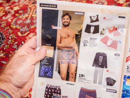 Foto de Paris, France - Dec 2, 2022: Man reading Auchan France leaflets supermarket chain selling underwear for men with special discount prices - Imagen libre de derechos