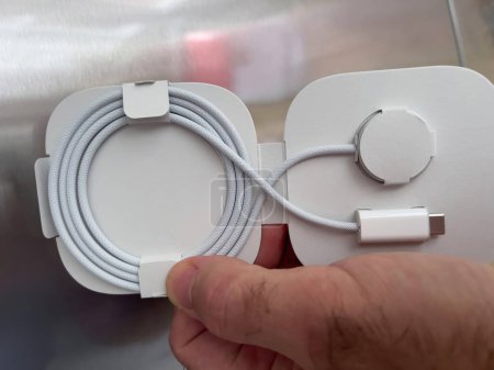 Foto de Paris, France - Oct 18, 2022: POV male hand holding against steel background cardboard box of new packaged Apple Watch Magnetic Fast Charger to USB-C cable - Imagen libre de derechos