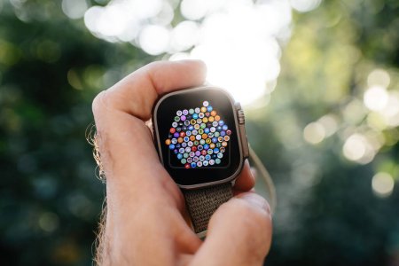 Foto de London, United Kingdom - Sept 28, 2022: Male hand holding new Apple Watch Ultra Smartwatch against defocused bokeh background with hundreds of apps on the oled display screen with great UI - Imagen libre de derechos