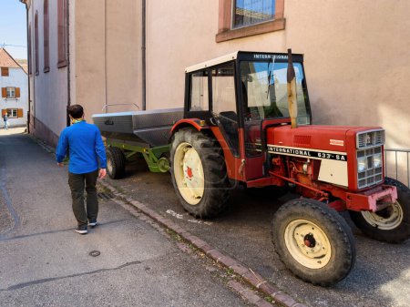 Foto de France - Sep 22, 2022: Rear view of farmer male walking near International 633-S vintage tractor with steel-case trailer - Imagen libre de derechos