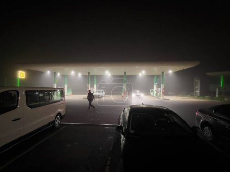Foto de France - Nov 11 2022: Male silhouette walking at night with gas station BP British Petroleum covered with fog - Imagen libre de derechos