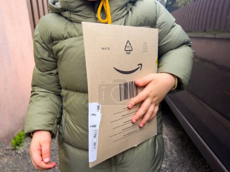 Photo for Luxembourg - Nov 8, 2022: male toddler holding Amazon Prime cardboard parcel box cardboard - fast delivery from the online retailer - Royalty Free Image