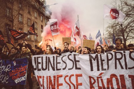 Téléchargez les photos : Strasbourg, France - Jan 19, 2023: Large crowd at protest with smoke greande in backgroun dholding placard marching against the French governments planned pension reform to push the retirement age - en image libre de droit