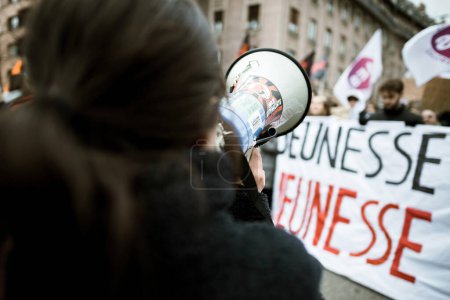 Téléchargez les photos : Strasbourg, France - Jan 19, 2023: Rear view of woman with Megaphone in front of Large crowd at protest against the French governments planned pension reform to push the retirement age from 62 to 64 - en image libre de droit