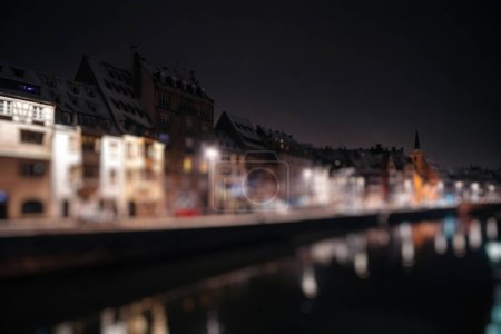 Foto de Defocused city of Strasbourg at night with illuminated houses facade near the Ill river - reflections of the buildings - Imagen libre de derechos
