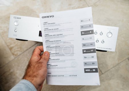 Téléchargez les photos : Paris, France - Oct 18, 2023: POV male hand holding paper safety information, and user manual of Onkyo BD-SP809 top-of-the-range Blu-ray deck - en image libre de droit
