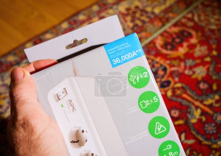 Téléchargez les photos : Frankfurt, Germany - Dec 2, 2022: POV male customer hand holding APC American Power Conversion Corporation by Schneider Electric cardboard package of new surge protector featuring 2 USB, 5 outlets and - en image libre de droit