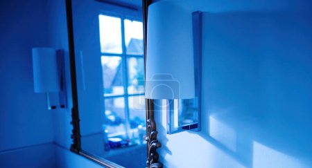 Photo for Blue color cast over bathroom boho-chic style mirror with two beautiful luminaires - Royalty Free Image
