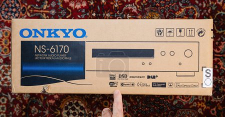 Photo for Paris, France - Dec 13, 2022: POV male hand pointing to cardboard package of new Onkyo NS-6170 network audio player with DSD Hi-Res Audio and DSD DAB plus WIFI device carpet rug silk background - Royalty Free Image