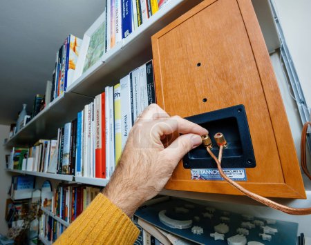 Foto de Paris, France - Dec 13, 2022: POV male hand connecting cable of Tannoy Mercury V1 bookshelf monitor speakers with quality cooper wire output terminal on the back - perspective view of Vitsoe 606 - Imagen libre de derechos