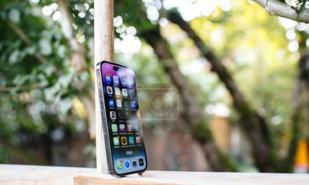 Photo for London, United Kingdom - Sept 28, 2022: Side view of new Apple Computers iPhone 14 pro on wooden surface with garden in background - retina oled display with new Dynamic island and all apps on home - Royalty Free Image