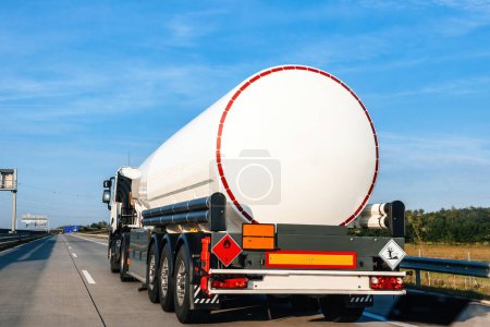 Photo for Rear view of a big fuel tanker truck driving on empty highway shipping fuel gas - clear blue sky in fast delivery cargo shipping of environmentally products.. - Royalty Free Image