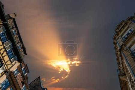 Photo for Low angle view of French alsatian timbered house and Haussmannian architecture with ray of light through storm sky in between them - Royalty Free Image