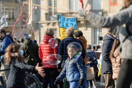 Téléchargez les photos : Strasbourg, France - Mar 6, 2022: Kids playing with soap bubbles as hundreds of demonstrators gathered in front of Russian Consulate in solidarity with Ukrainians and against the war after Russian - en image libre de droit