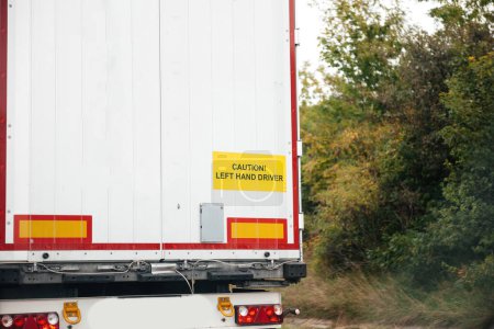 Foto de Caution, left hand driver signage on a white cargo truck driving on highway - fast parcel cargo delivery - Imagen libre de derechos