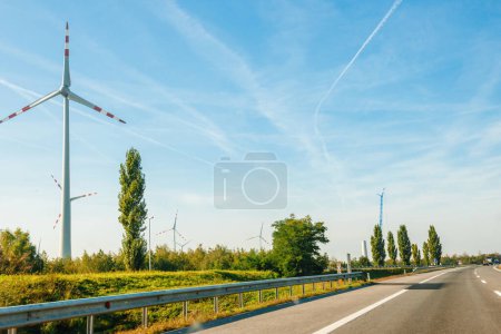 Téléchargez les photos : Grande autoroute moderne dans un grand parc d'éoliennes produisant de l'électricité au-dessus de la forêt avec grue en installant une autre en arrière-plan - en image libre de droit