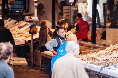 Téléchargez les photos : Thessalonique, Grèce - 30 oct. 2014 : Pêcheur attendant des clients au marché aux poissons en arrière-plan achetant des poissons de la mer et d'autres spécialités - en image libre de droit