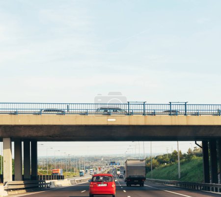 Téléchargez les photos : Hongrie - 30 sept. 2014 : Voiture rouge conduite rapide sous le pont avec plusieurs voitures sur l'autoroute hongroise - Kia Picanto conduite - en image libre de droit