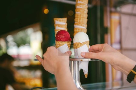 Téléchargez les photos : Femme faisant des emplettes de crème glacée sur un cône de gaufre chaud avec du yaourt et de la crème glacée rouge cerise sur le comptoir - en image libre de droit
