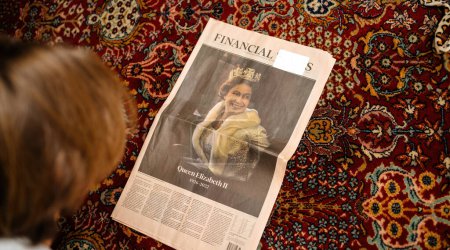 Foto de París, Francia - 09 / 09 / 2022: Mujer leyendo en el sofá de la sala de estar la última portada del periódico Le Figaro rindiendo homenaje a la reina después de su muerte - La reina Isabel II murió en el castillo de Balmoral en - Imagen libre de derechos