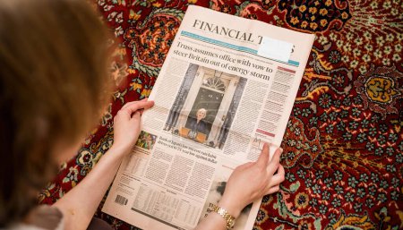 Foto de LONDRES, INGLATERRA - 20 DE OCTUBRE: Mujer de primer plano leyendo en el piso de la sala de estar la portada del Financial Times anunciando la renuncia de la Primera Ministra Liz Truss, en Westminster - Imagen libre de derechos
