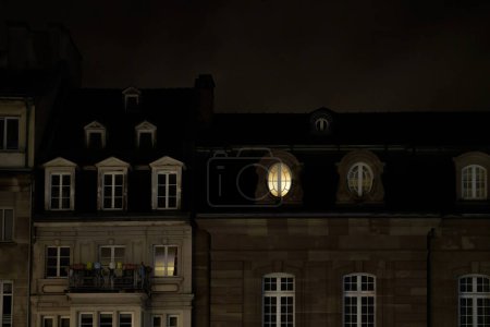 Téléchargez les photos : Immeuble de luxe avec une seule fenêtre ovale éclairée à partir de l'intérieur- travailler tard dormir tard - immeuble d'appartements de luxe - en image libre de droit