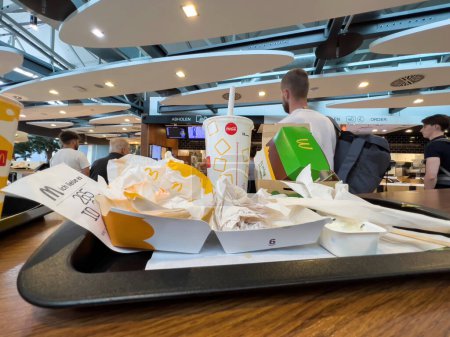 Photo for Frankfurt, Germany - Aug 17, 2022: Tray with waste from Fast-Food inside McDonalds restaurant at Frankfurt International Airport - background with customer at the collect point - Royalty Free Image