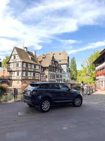 Foto de Estrasburgo, Francia - Aug 2, 2022: Lujo Range-Rover coche suv negro estacionado en el centro de la ciudad de Estrasburgo petite-France con casas de madera tradicionales en el fondo y el canal del río enfermo - Imagen libre de derechos
