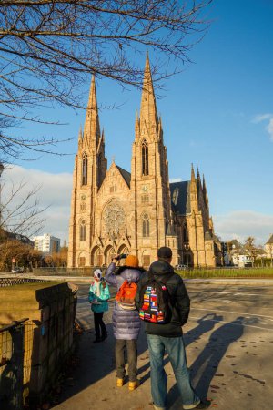 Téléchargez les photos : Strasbourg, France - 1 Ap 2015 : Un groupe d'hommes et de femmes se rassemblent devant une majestueuse église St paul - Bâtiment religieux, un lieu où leurs croyances s'expriment richement à travers son architecture - en image libre de droit