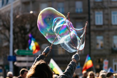Foto de En un festival vibrante, burbujas multicolores llenan el aire mientras alguien en la multitud los sopla con una varita de burbujas: cada orbe líquido de alegría frágil capturado en el aire y centrado en el primer plano. - Imagen libre de derechos