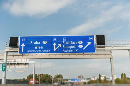 Photo for Defocused blur view of highway beneath a sky filled with clouds, passing an roadsign for directions the cities of Wien, Praha and Budapest - Royalty Free Image