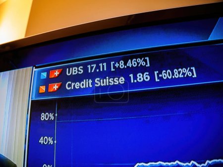 Foto de Bael, Suiza - 19 de marzo de 2023: Primer plano de un canal de noticias televisivo con información de acciones diversa mientras los inversionistas digieren la noticia de la adquisición histórica de UBS de Credit Suisse Group AG - Imagen libre de derechos