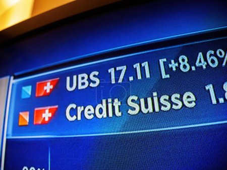 Foto de Basilea, Suiza - 19 de marzo de 2023: Primer plano de un canal de noticias televisivo con diversos precios bursátiles de UBS y Credit Suisse - Imagen libre de derechos