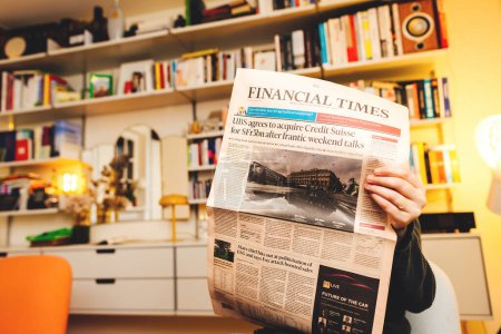 Téléchargez les photos : Paris, France - 20 mars 2023 : Le Financial Times annonce l'acquisition historique par UBS de la rivale Credit Suisse Group AG - une femme liseuse dans son salon avec Vitsoe 606 - en image libre de droit